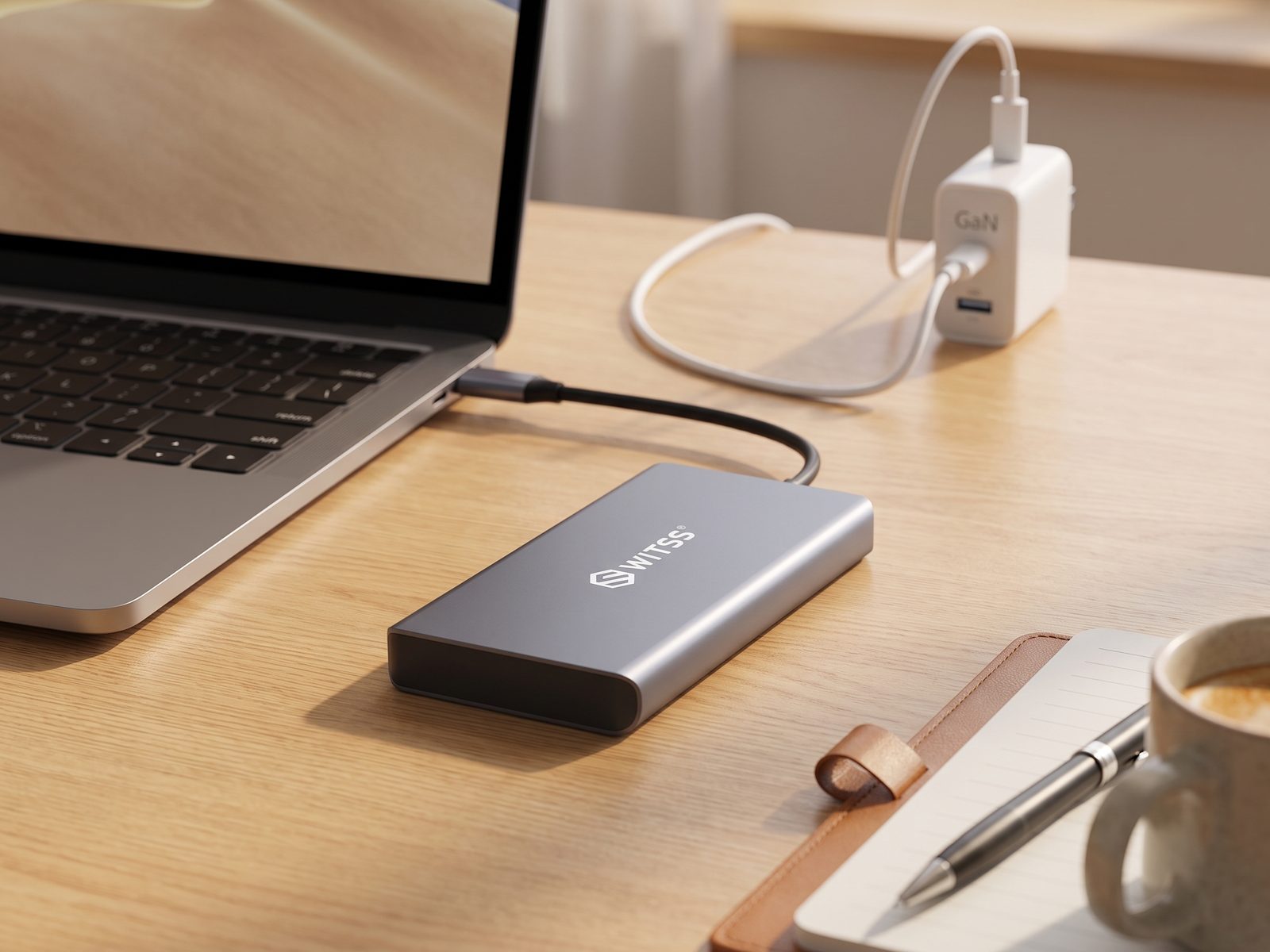 Switss® 12-in-1 hub on a desk, laptop charging cable running from a GaN charger in the background