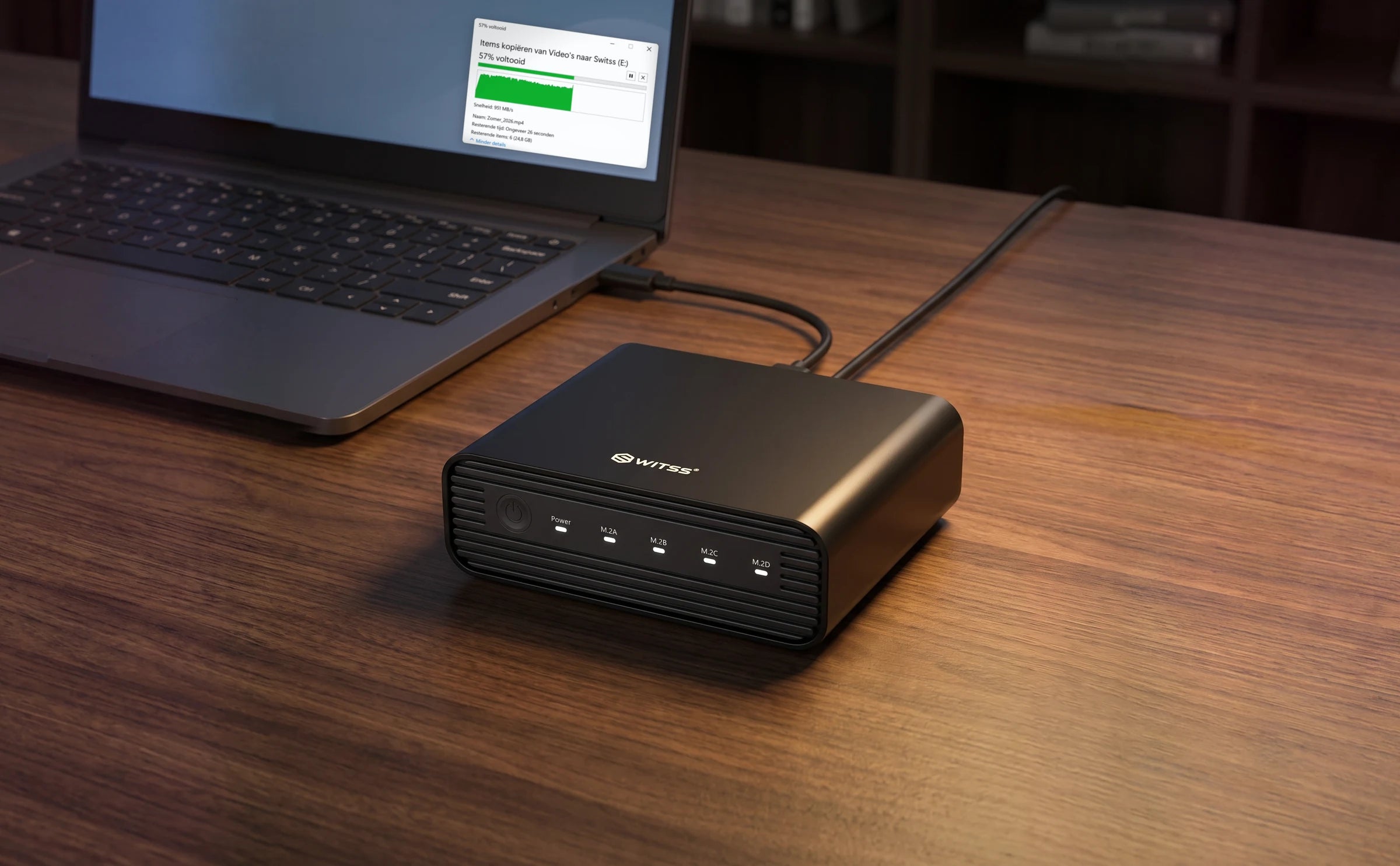 De Switss 4-Bay M.2 behuizing met de USB-C-kabel aan een laptop en de stroomkabel aangesloten, met op het scherm het venster van een lopende kopie naar de schijf