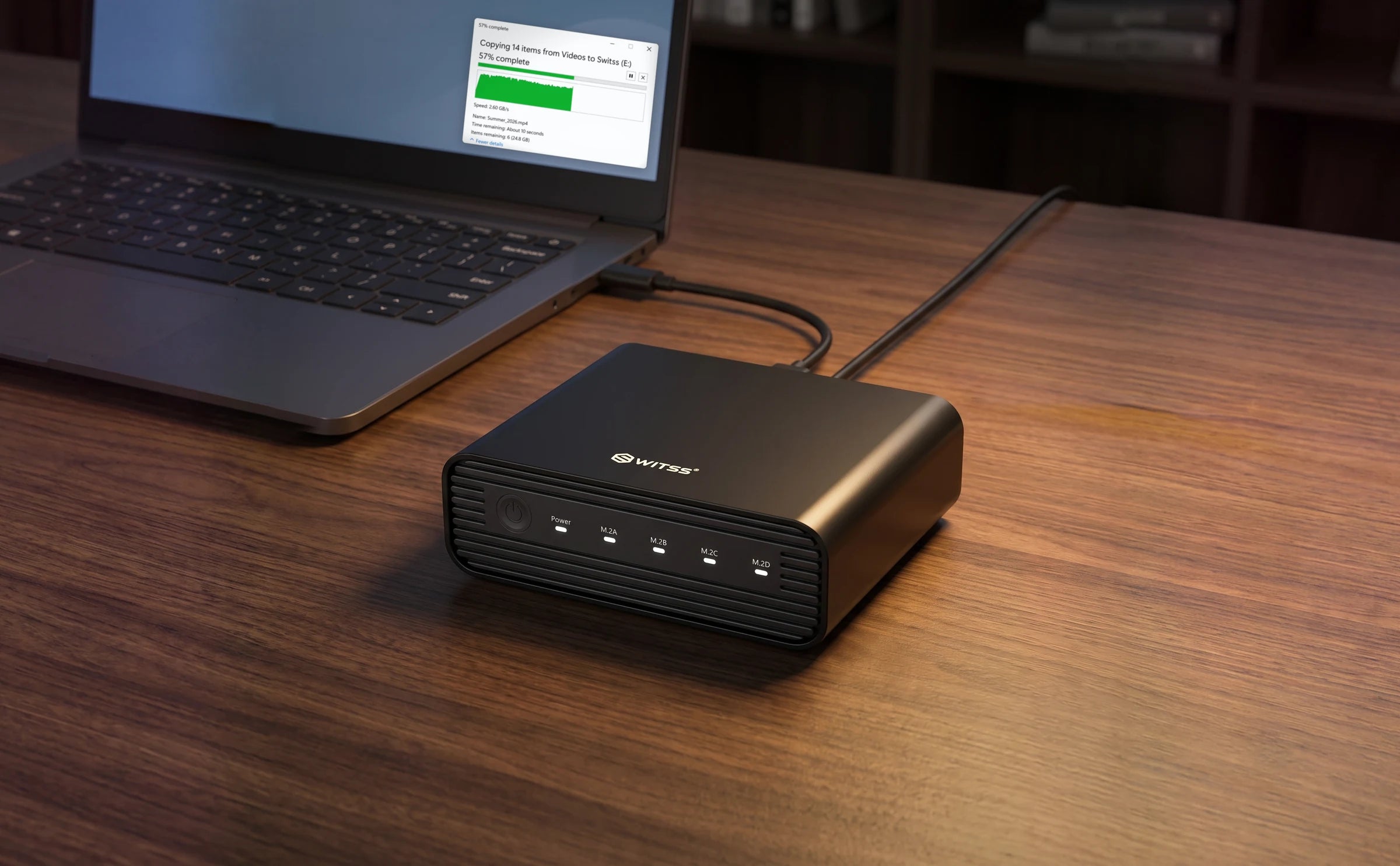 The Switss 4-bay M.2 enclosure with the USB-C cable running to a laptop and the power cable connected, with a file copy to the drive in progress on the screen