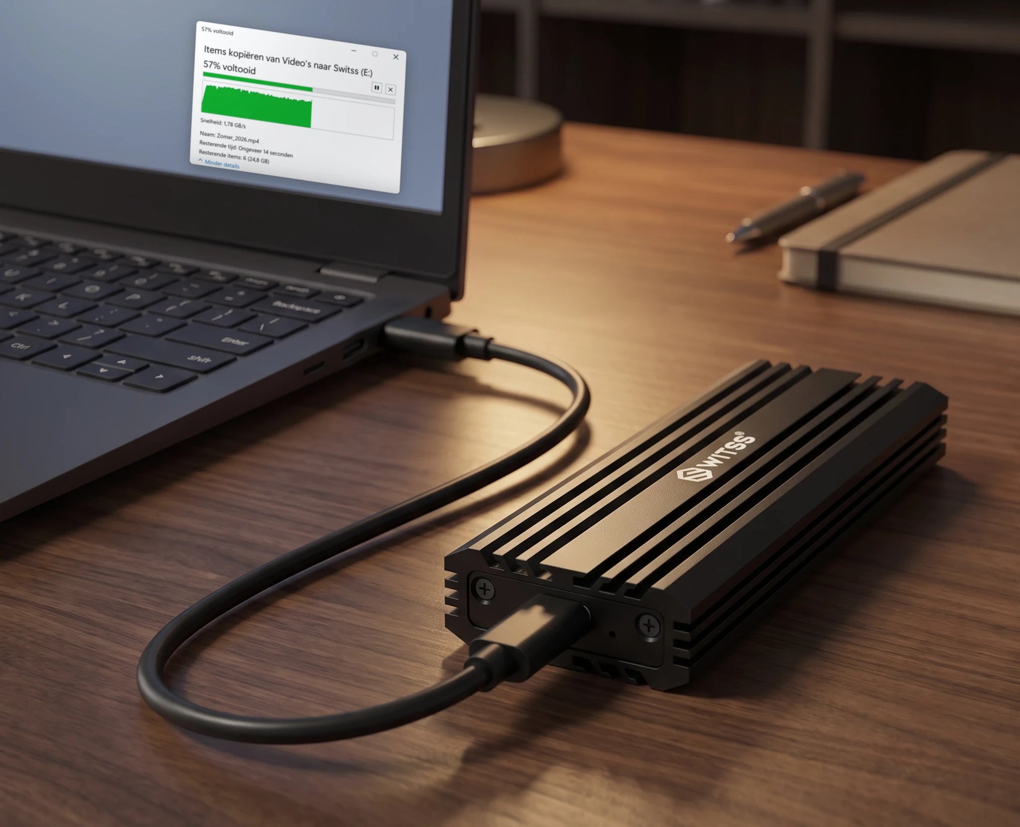 De Switss M.2 behuizing met de USB-C-kabel aan een laptop, met op het scherm het venster van een lopende kopie naar de schijf