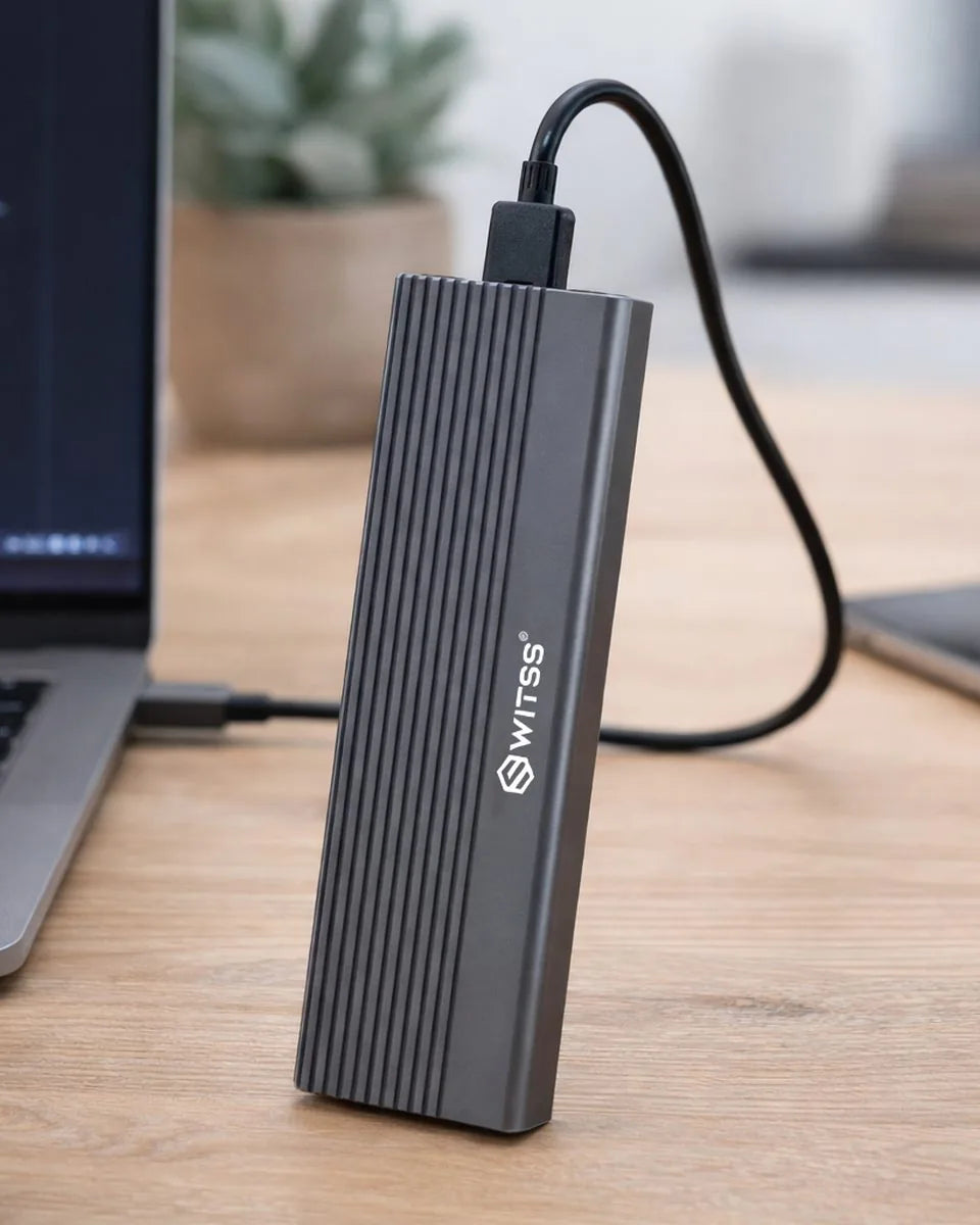 Switss M.2 SSD enclosure standing upright on a desk, with the cable connected to a laptop