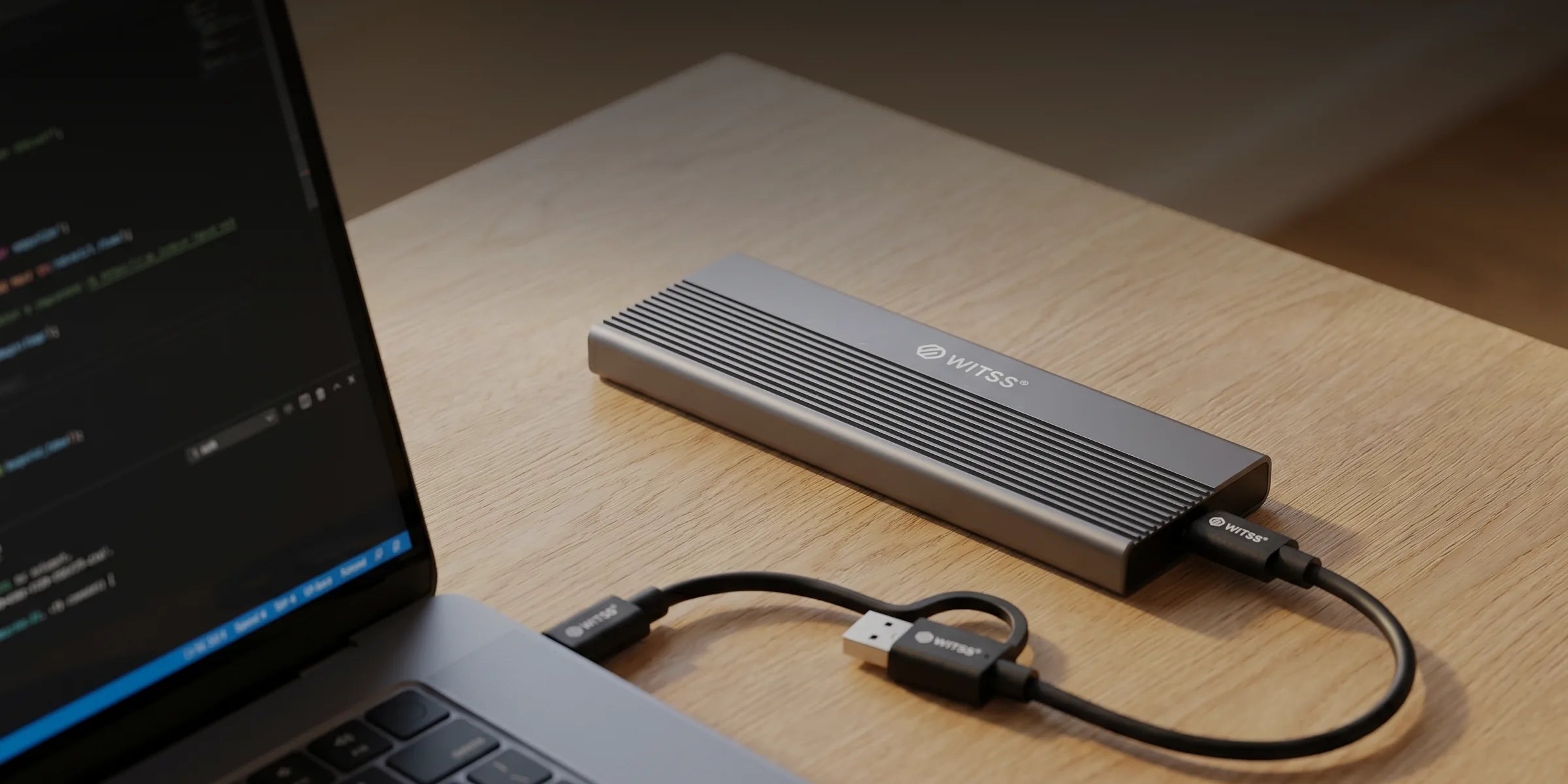 The M.2 enclosure on a wooden desk, connected to a laptop with the USB-C cable, in evening light