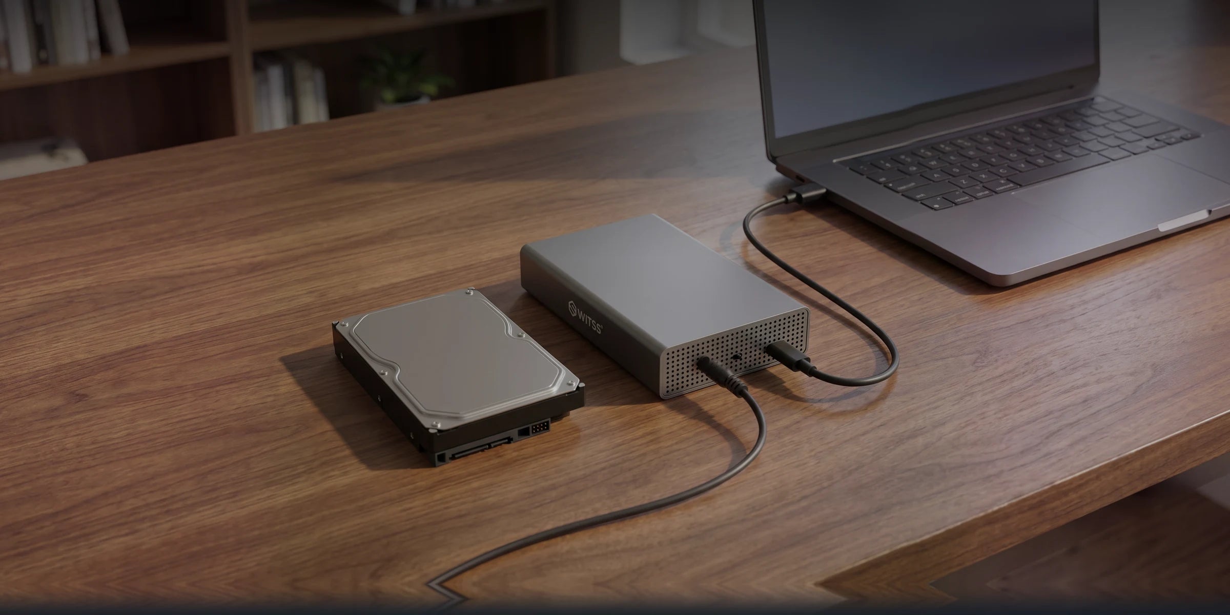 De Switss 3,5 inch behuizing op een houten bureau naast een losse harde schijf, met de USB-kabel naar een laptop en de netvoeding aangesloten